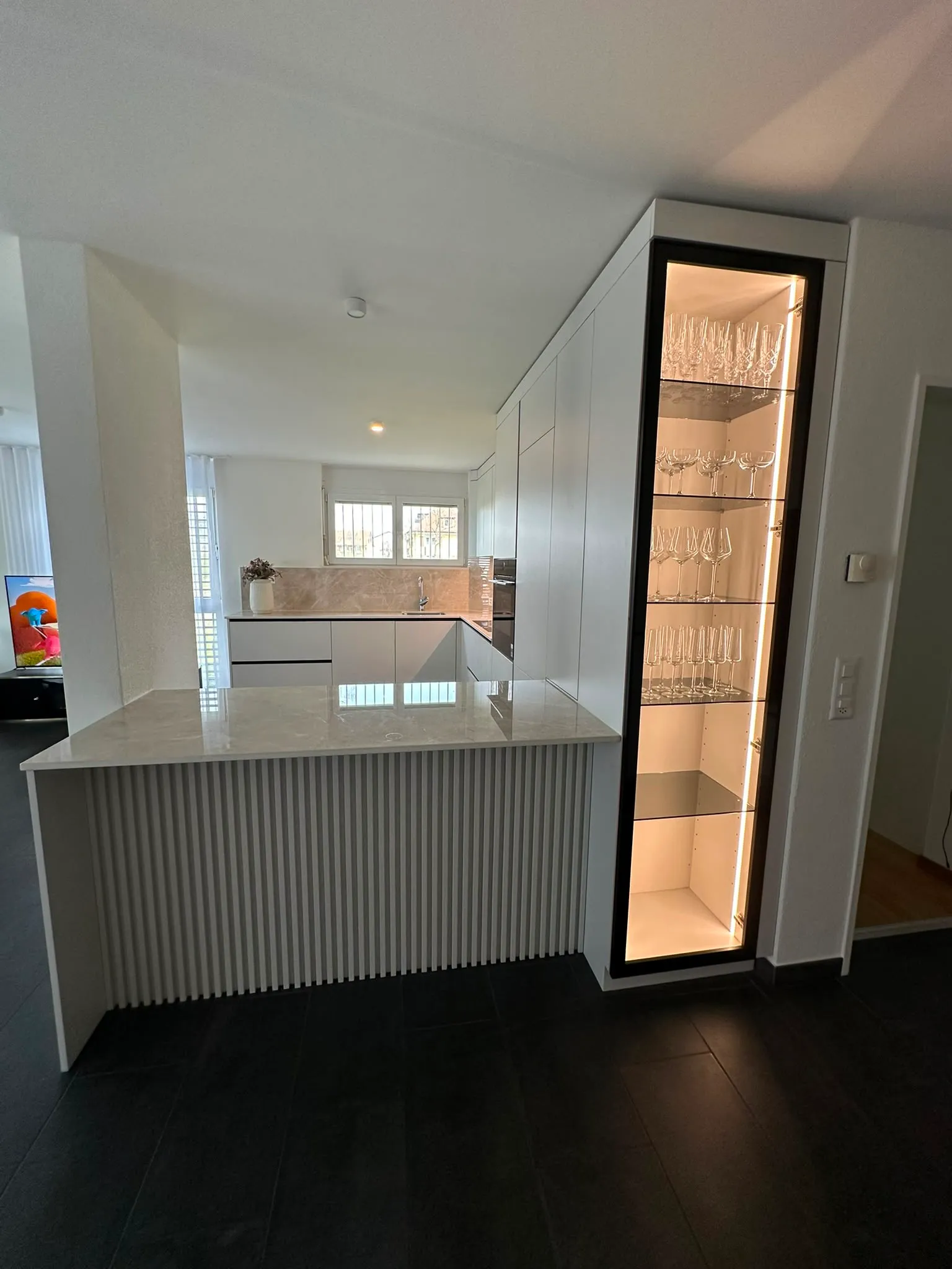 Weisse Küche mit Halbinsel und beleuchteter Glasvitrine